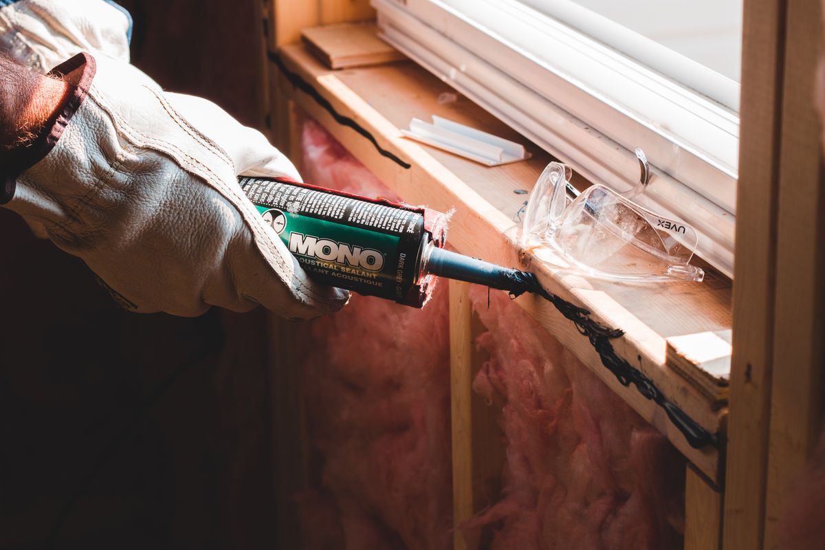 A gloved hand applying sealant from a cartridge gun along a joint